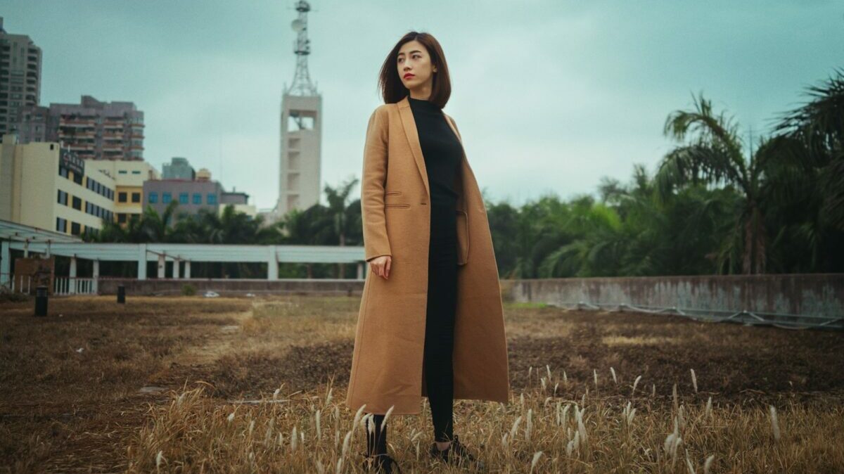 woman wearing brown coat standing on brown grass